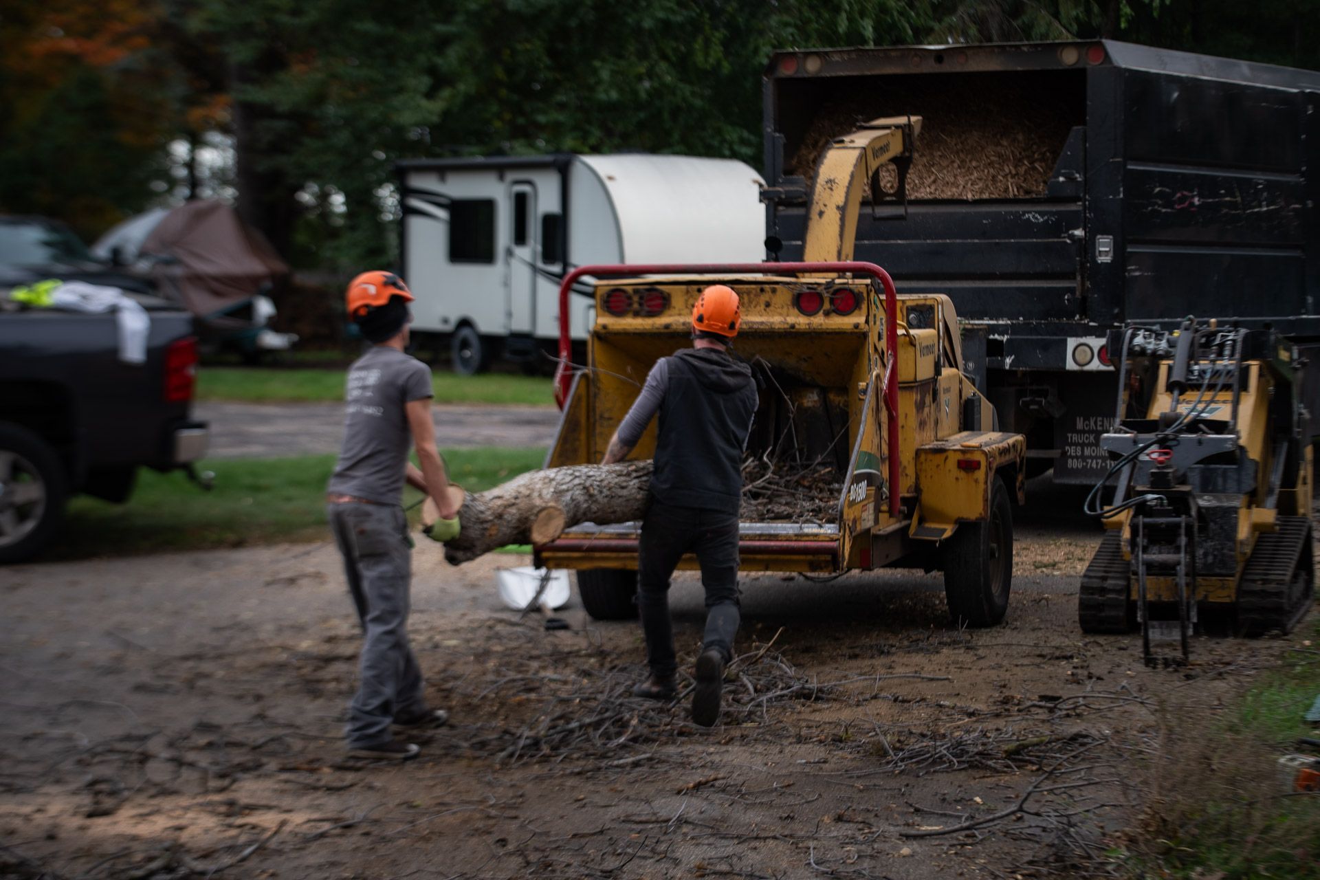 Workers load debris into a dump truck beside a yellow loader on a muddy construction site.