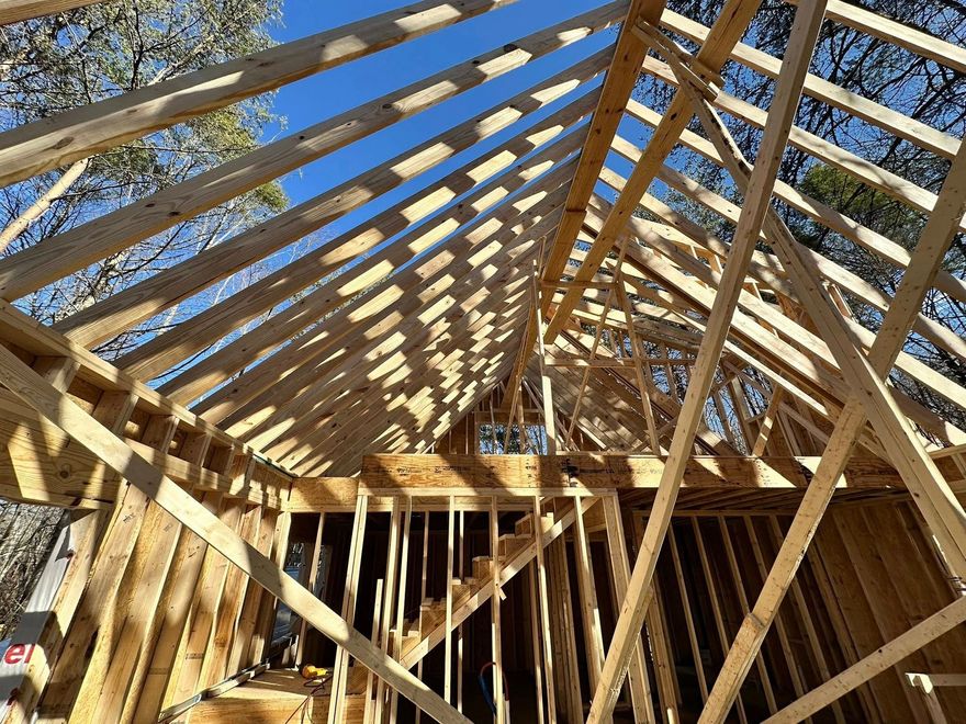 Wooden house frame under construction with exposed roof trusses against a blue sky.