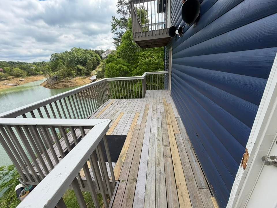 Wooden deck beside a blue house overlooking a river and trees under cloudy skies