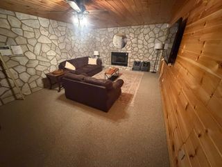 Cozy living room with stone walls, wood paneling, beige carpet, brown couch, fireplace, and wall-mounted TV