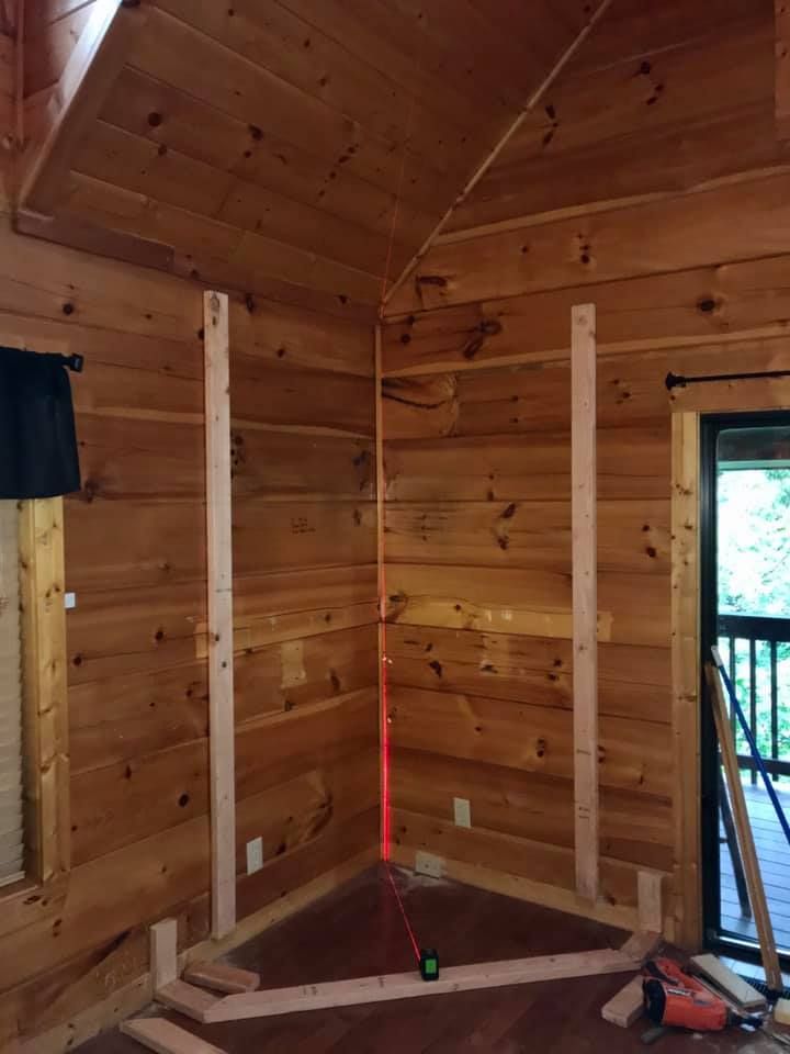 Wood-paneled room with wall studs and a red level on the floor, as if framing a corner.