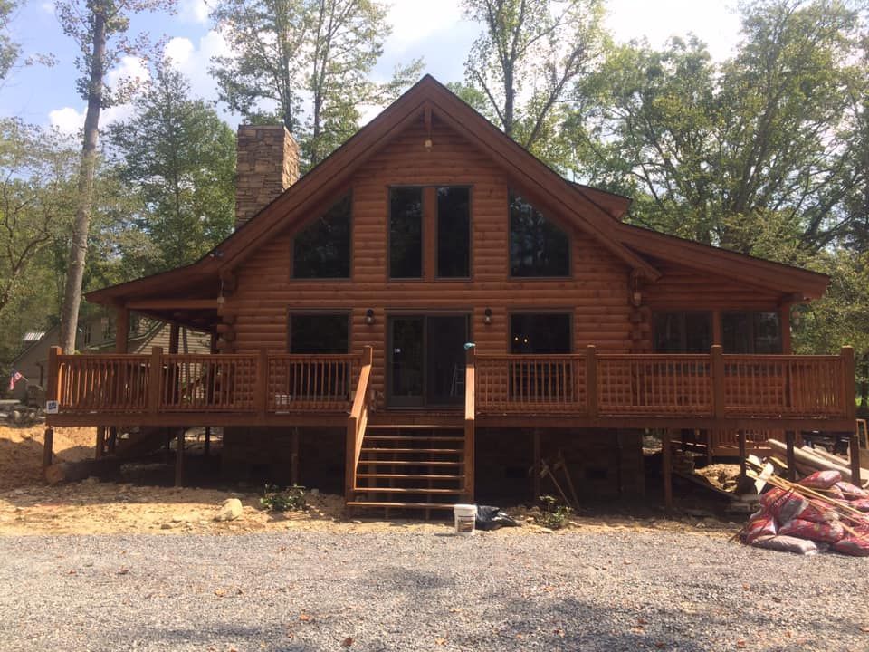 Log cabin with a front porch and stairs, surrounded by trees and gravel in a wooded setting