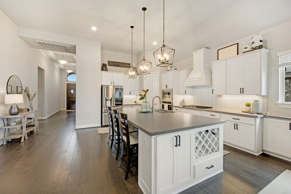 Bright modern kitchen with white cabinets, island, pendant lights, and dark wood floors