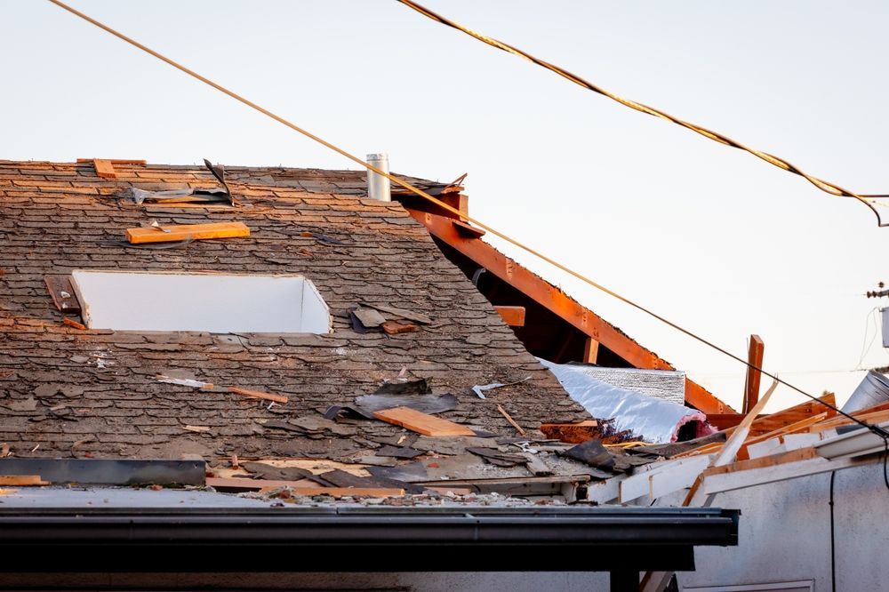 Damaged shingled roof with missing tiles and exposed wooden beams under overhead power lines