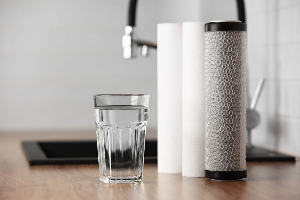 Glass of water beside a white-and-gray water filter on a kitchen counter