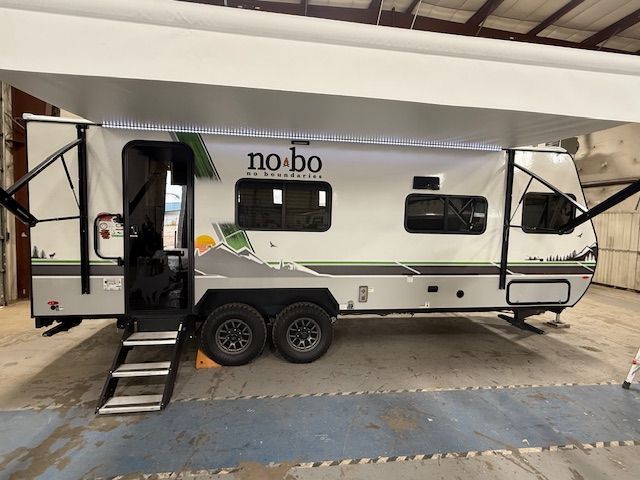 A gray and white No Boundaries travel trailer with awning extended, parked indoors.