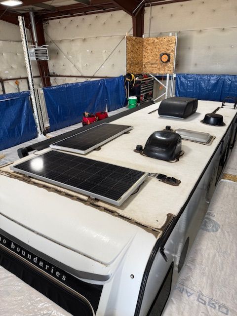 White RV roof with two solar panels, vent covers, in a garage.