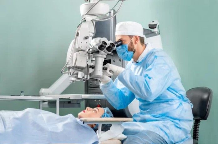 A surgeon in protective medical gear operates on a patient using a specialized eye microscope in a sterile clinic.