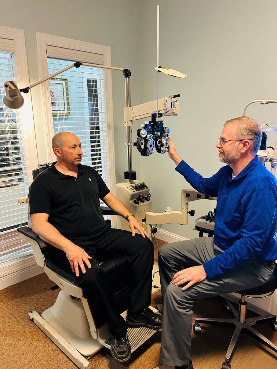 Optometrist examining a seated patient in an eye exam room with a vision testing device in Hope Mills, NC.