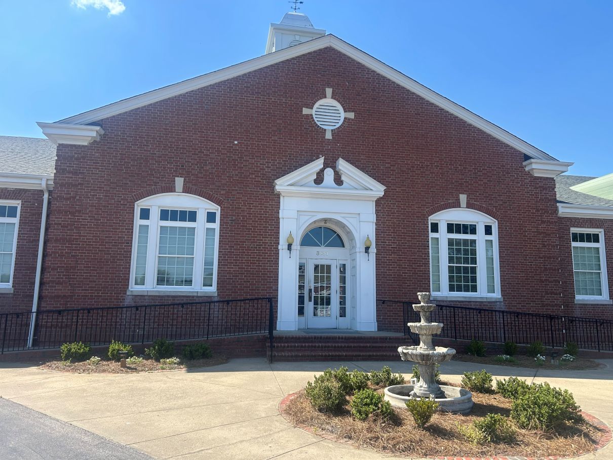 Red brick building facade with white-trimmed windows, central doorway, and small fountain in front in Eastover, NC.