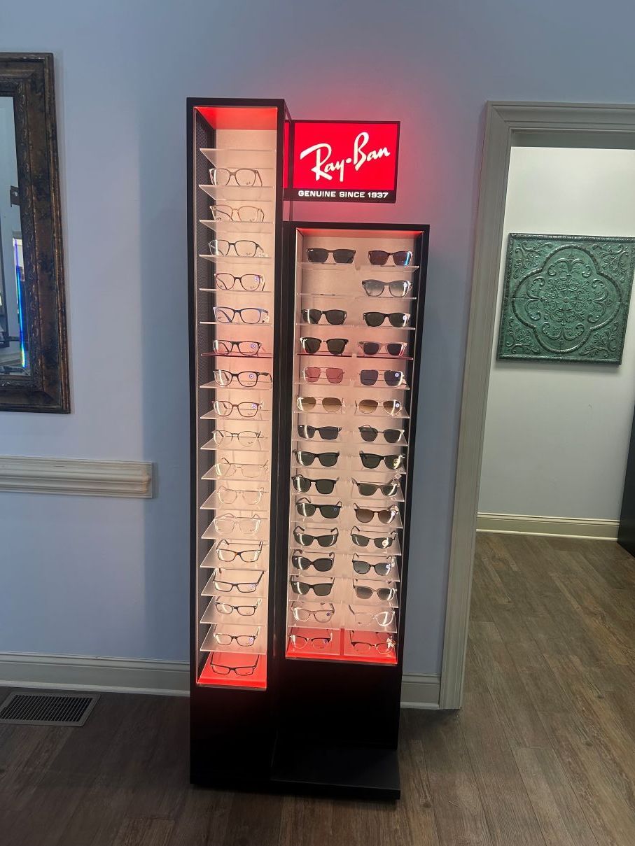 Ray-Ban eyeglass display stand with red-lit shelves and sunglasses in a store corridor in Eastover, NC.