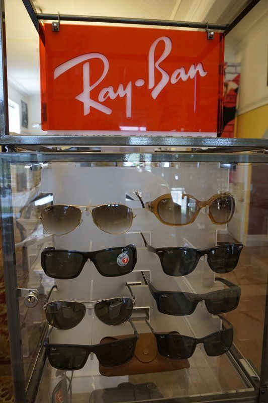 A glass display case containing eight pairs of Ray-Ban sunglasses, topped with a red logo sign.