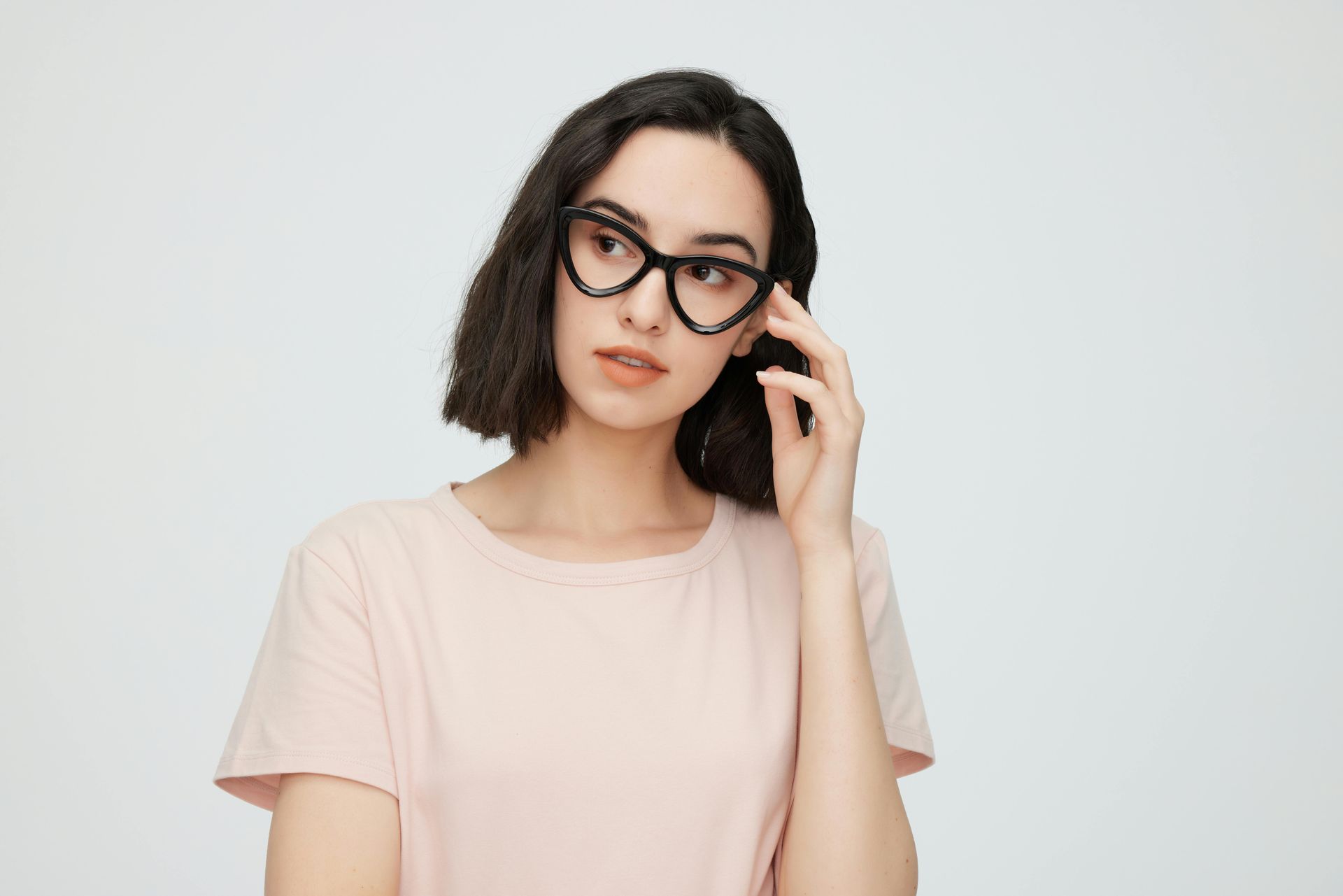 A person with short dark hair wears black, heart-shaped glasses while looking to the side against a neutral background.