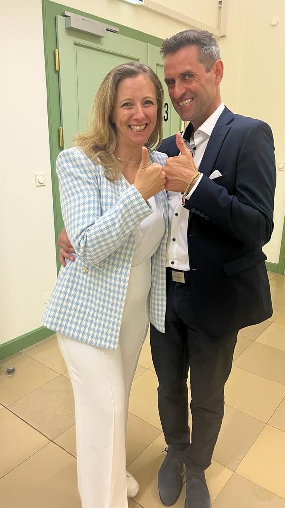 A man in a suit and a woman in white pants are posing for a picture.