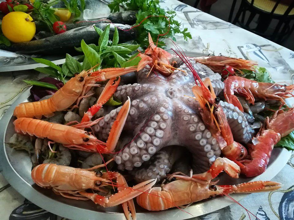 Un grosso polpo crudo circondato da scampi e gamberi su un piatto da portata in metallo con verdure.