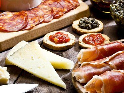 Un piatto di salumi assortiti, tra cui affettati sottili, spicchi di formaggio e cracker con vari condimenti.