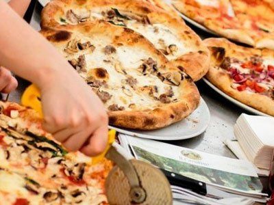 Una mano usa una rotella tagliapizza per affettare una pizza