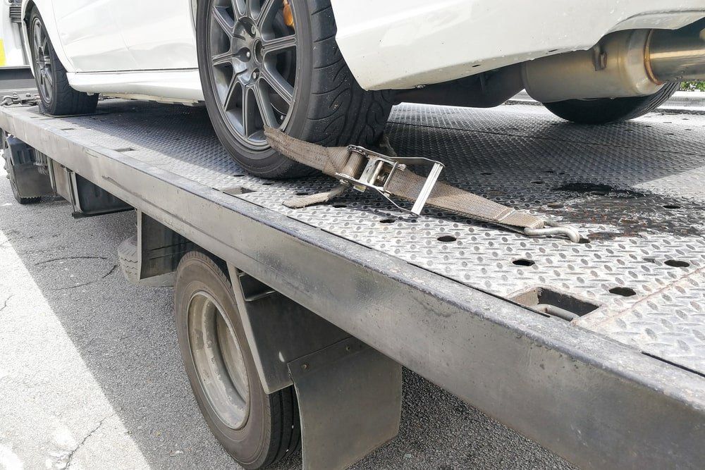 A white car is being towed by a tow truck.