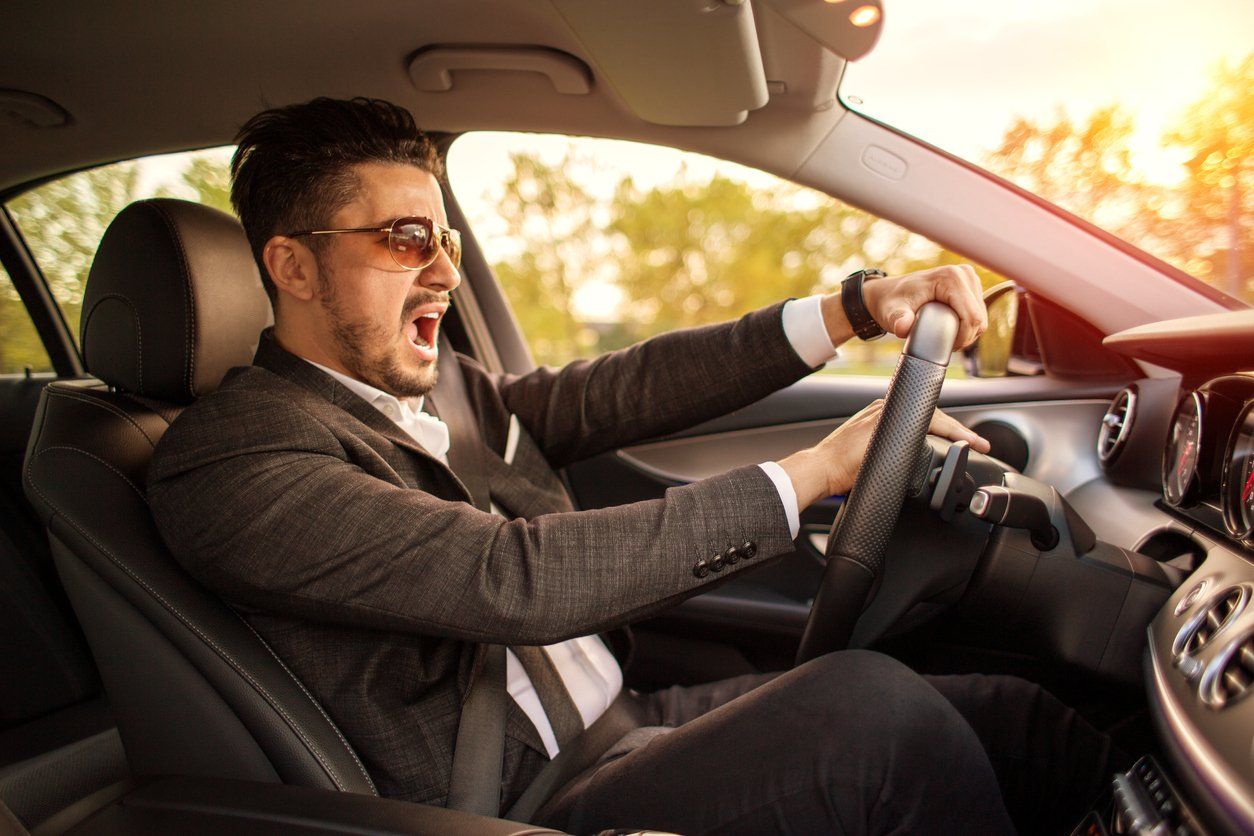 A man in a suit and tie is driving a car and screaming.