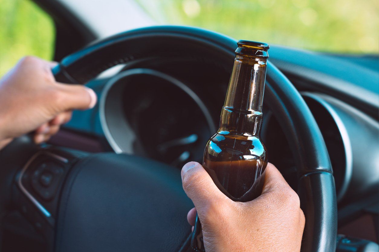 A person is holding a bottle of beer while driving a car.