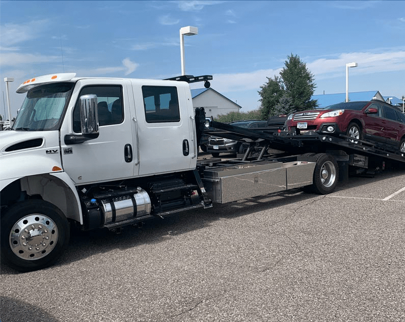 A tow truck is towing a red car in a parking lot.
