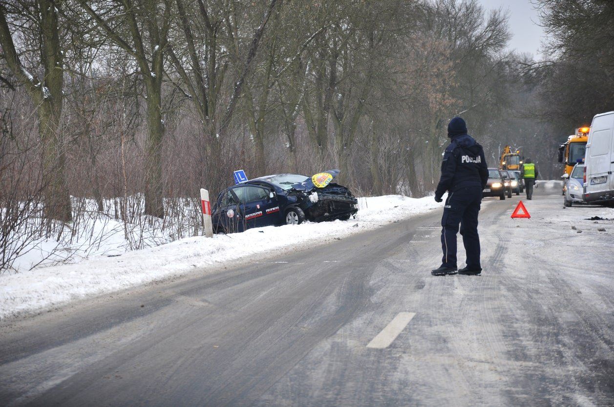 A man is standing on the side of a snow covered road.