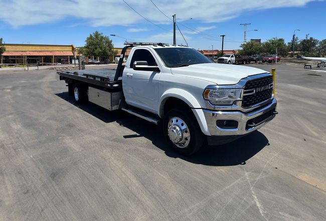 A white tow truck is parked in a gravel lot in front of a building.