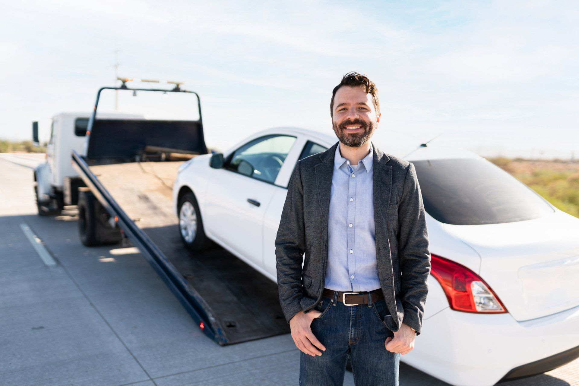 A man is standing in front of a tow truck with a car on it.