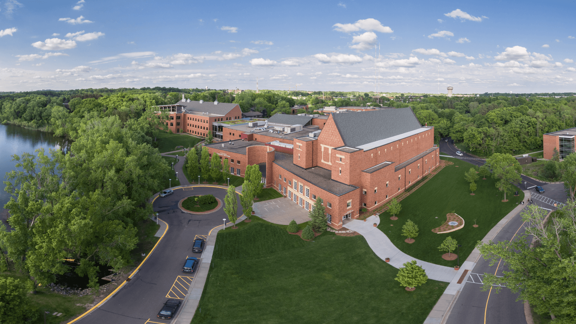 An aerial view of a large brick building surrounded by trees and a lake.