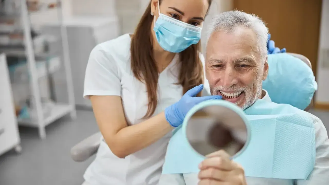Patient bekommt seine neuen Zähne im Spiegel gezeigt.