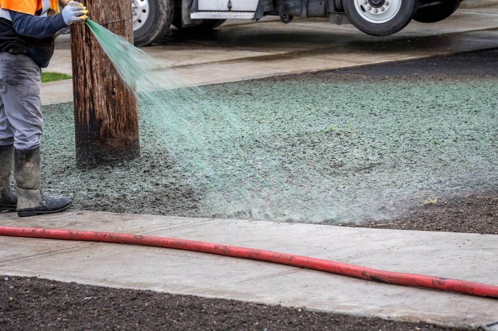Worker spreading green material on a wet road near a curb
