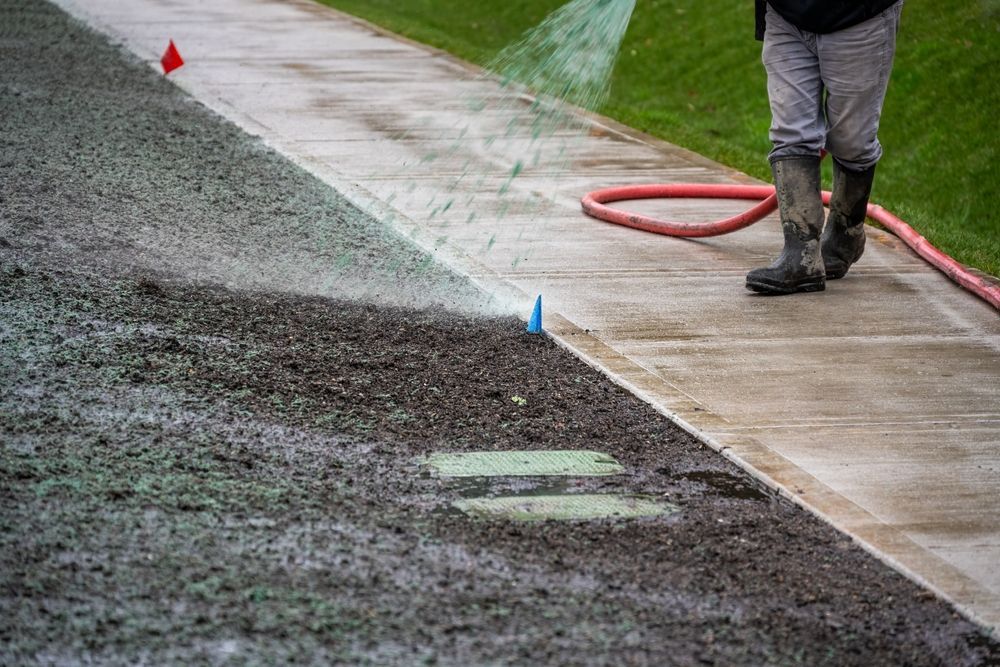 Worker in boots standing on wet pavement beside a gravel shoulder and red hose barriers