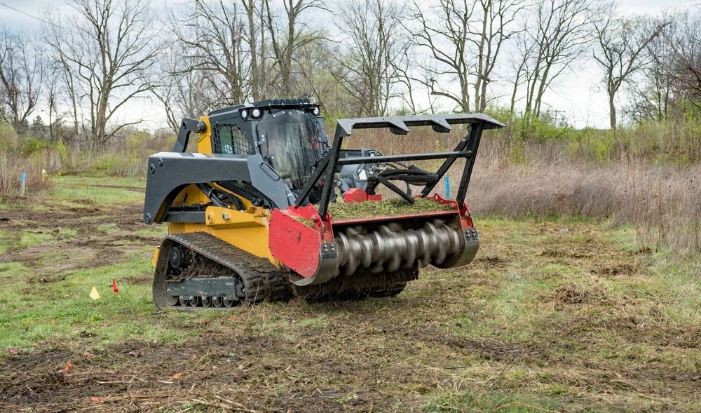 Tracked mulching machine in a grassy field with leafless trees behind it