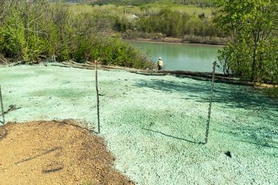 Green mineral pool with a person standing by the water in a wooded outdoor area