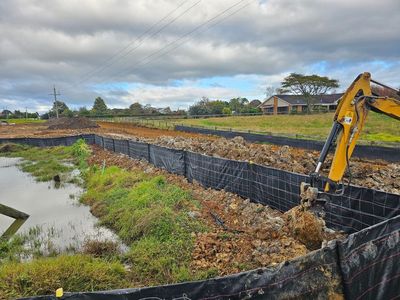 Excavator building a riverbank retaining wall beside a waterway under cloudy skies