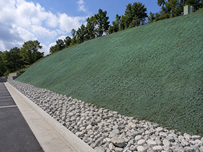 Steep green embankment reinforced with rocks beside a road under a blue sky