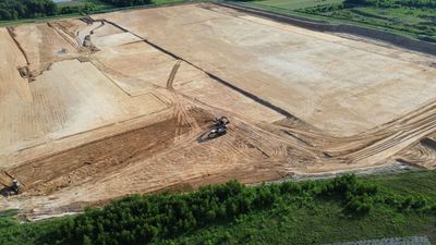 Aerial view of a large tan dirt construction site with graded fields and green vegetation along the edge