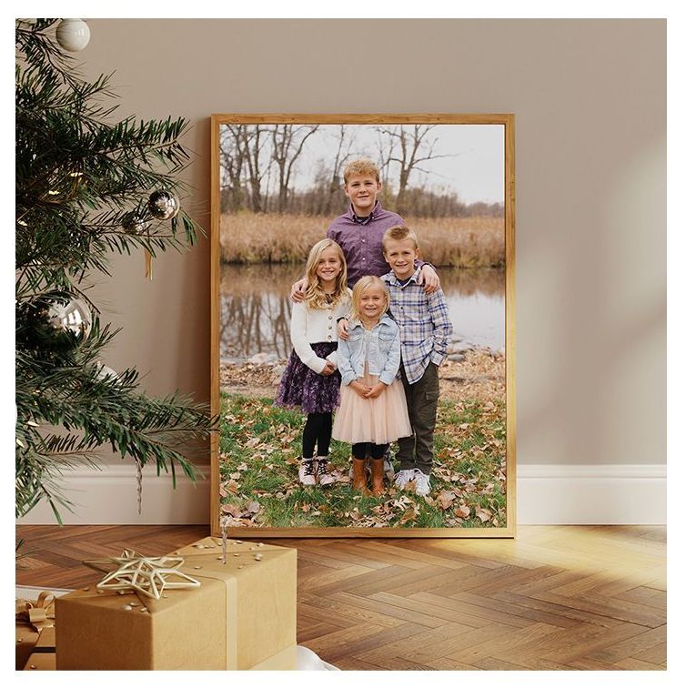 Framed family portrait leaning by a Christmas tree and wrapped gift on a wooden floor