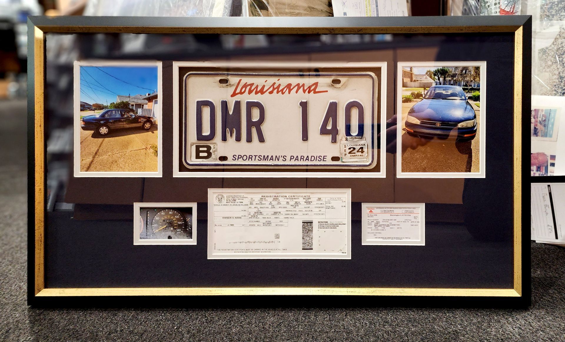 Framed Louisiana license plate display with car photos and paperwork on a black-and-gold background