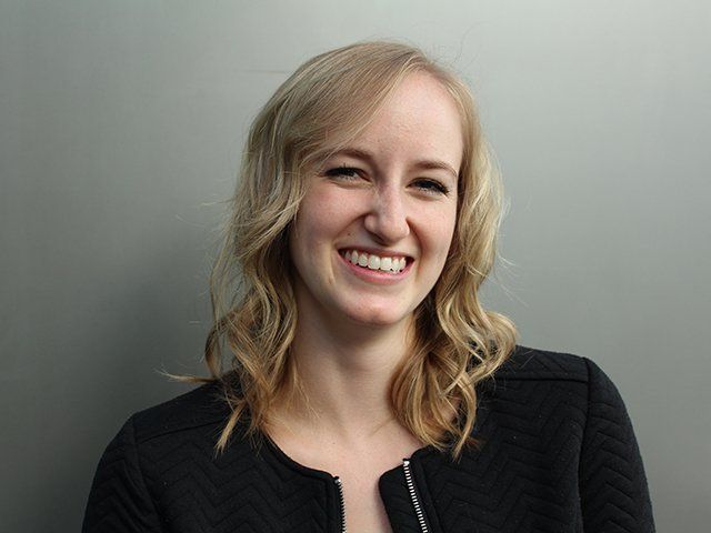 Smiling person with wavy blonde hair against a plain gray background