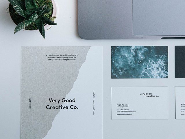 Minimalist creative brand mockup on a desk with laptop, plant, and blue-gray print designs