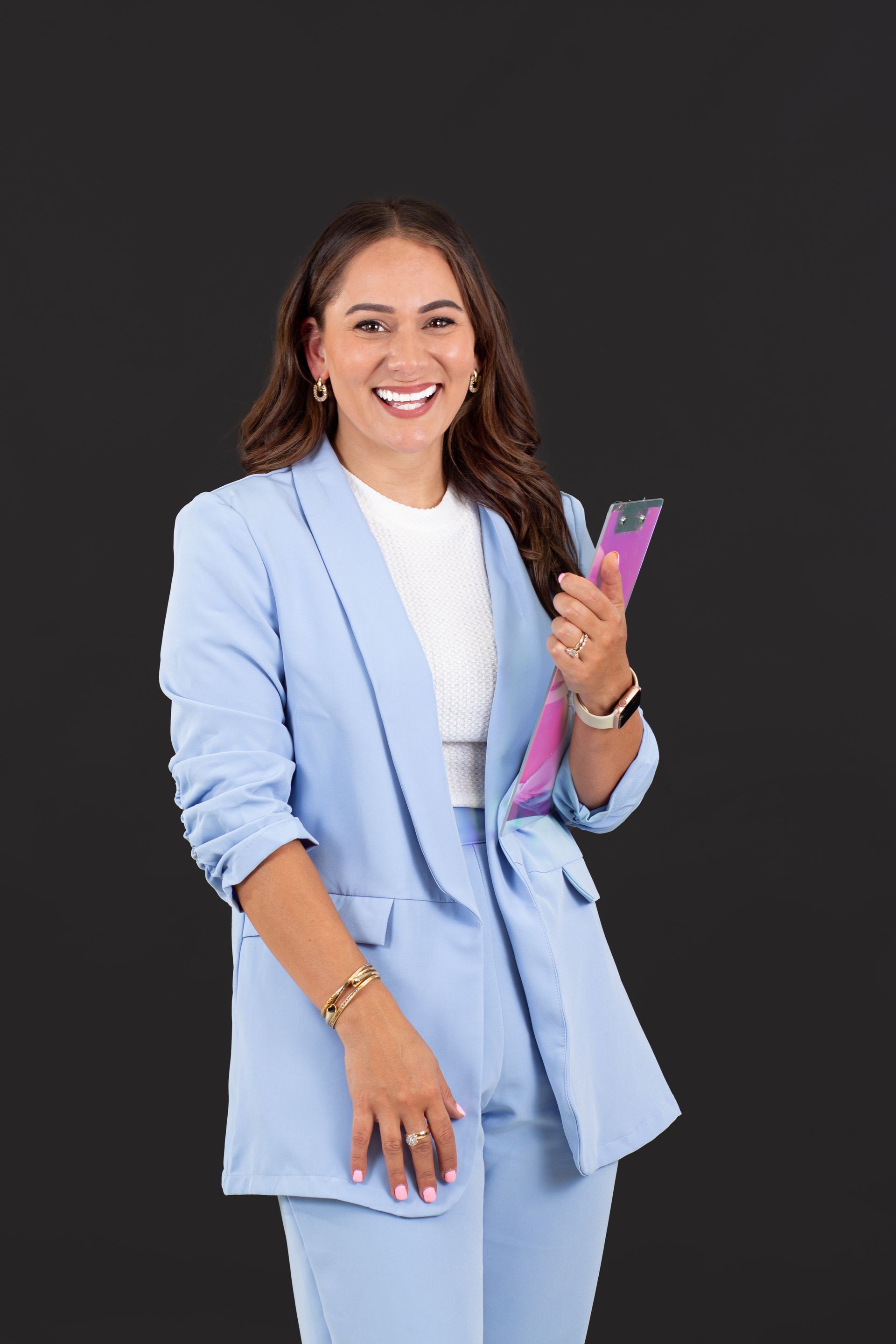 Woman in a light blue suit smiling and holding a smartphone against a dark background