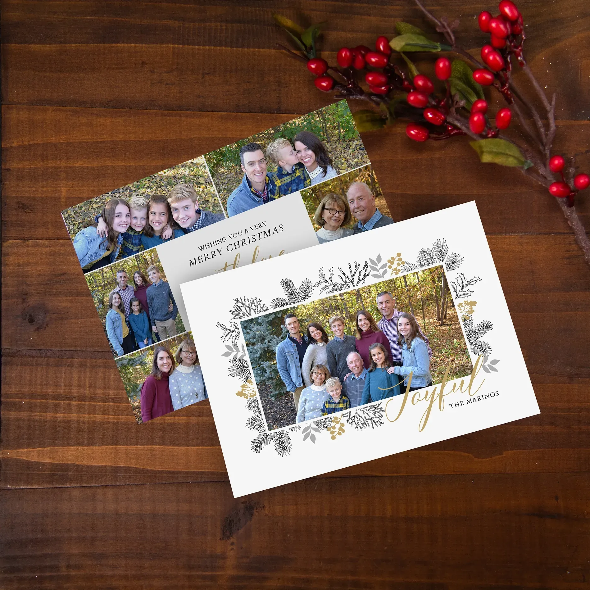 Holiday greeting cards with family photos on a wooden table, decorated with red berries and greenery