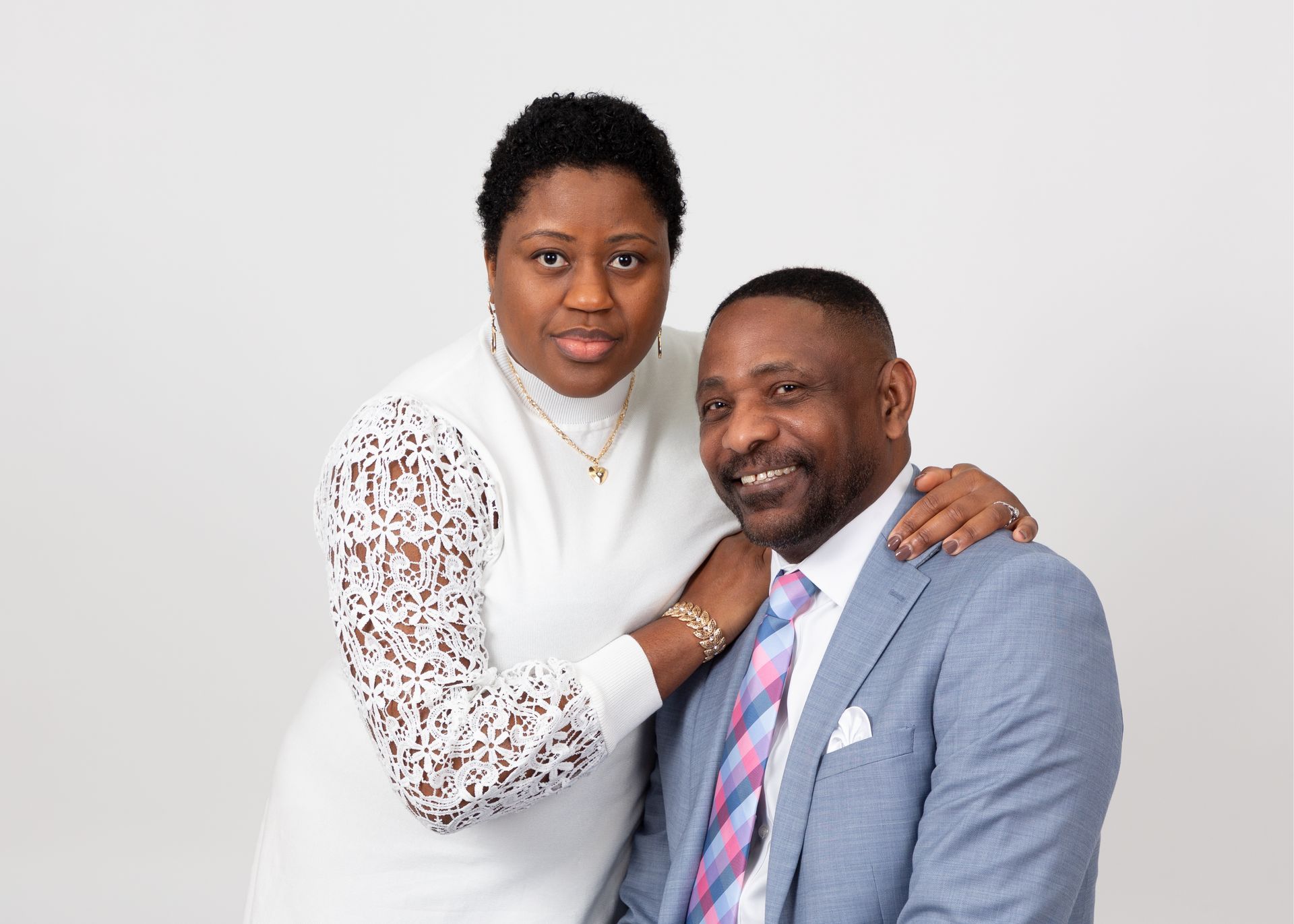Couple posing together against a white background, the woman resting her hand on the man's shoulder.