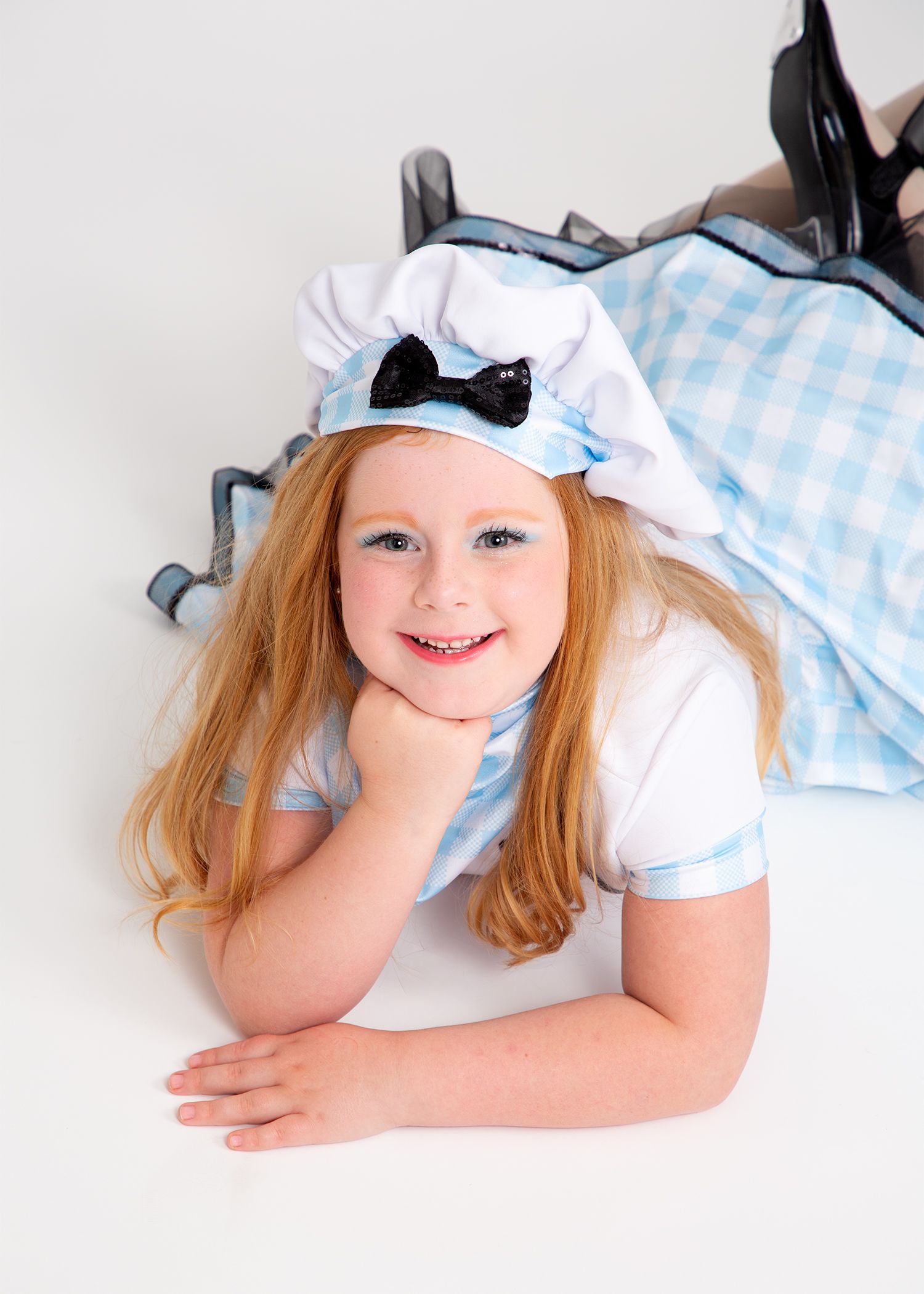 Child in a blue-and-white dress and bonnet lies on her stomach, smiling at the camera.