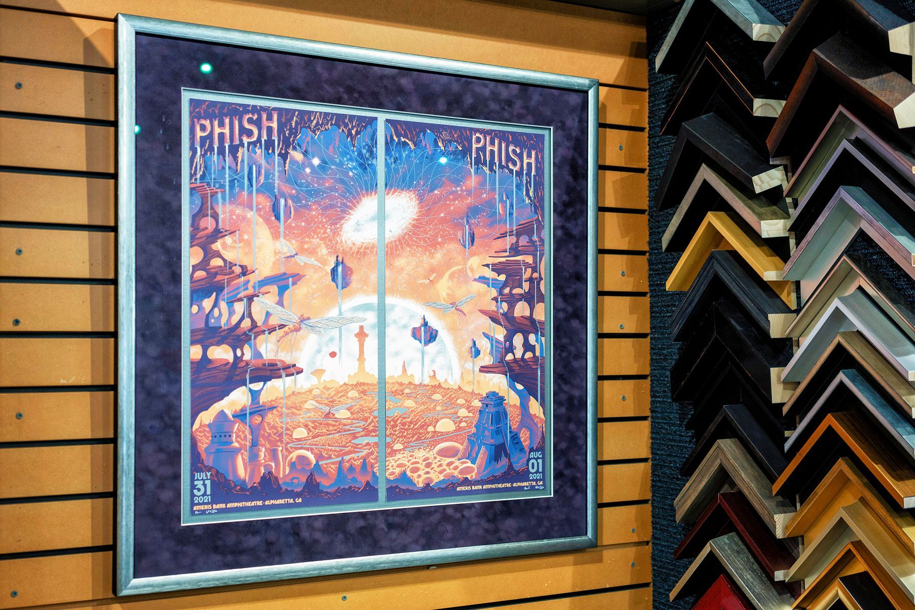Framed Phish poster on a wood wall beside stacked picture frames