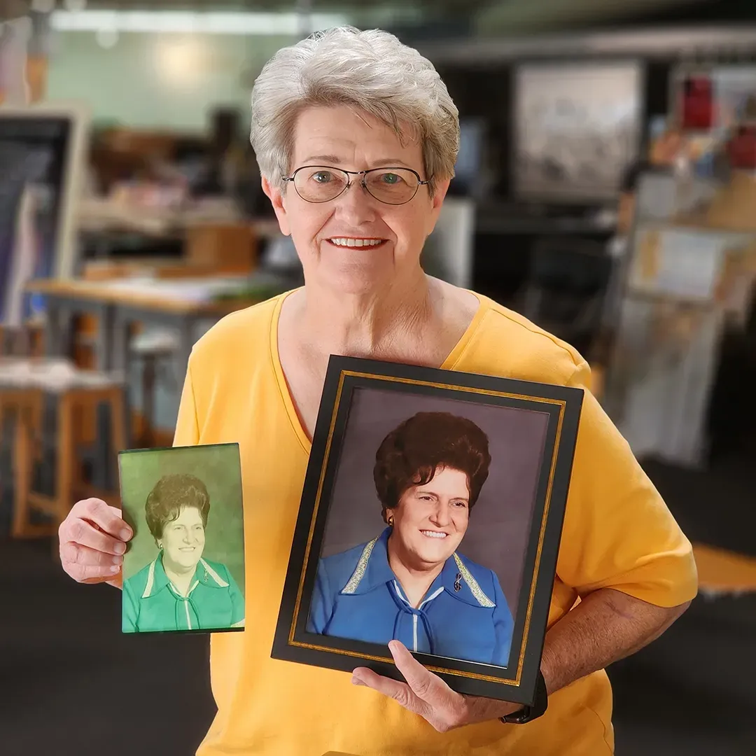 Woman in a yellow shirt holding two framed portraits in an art studio