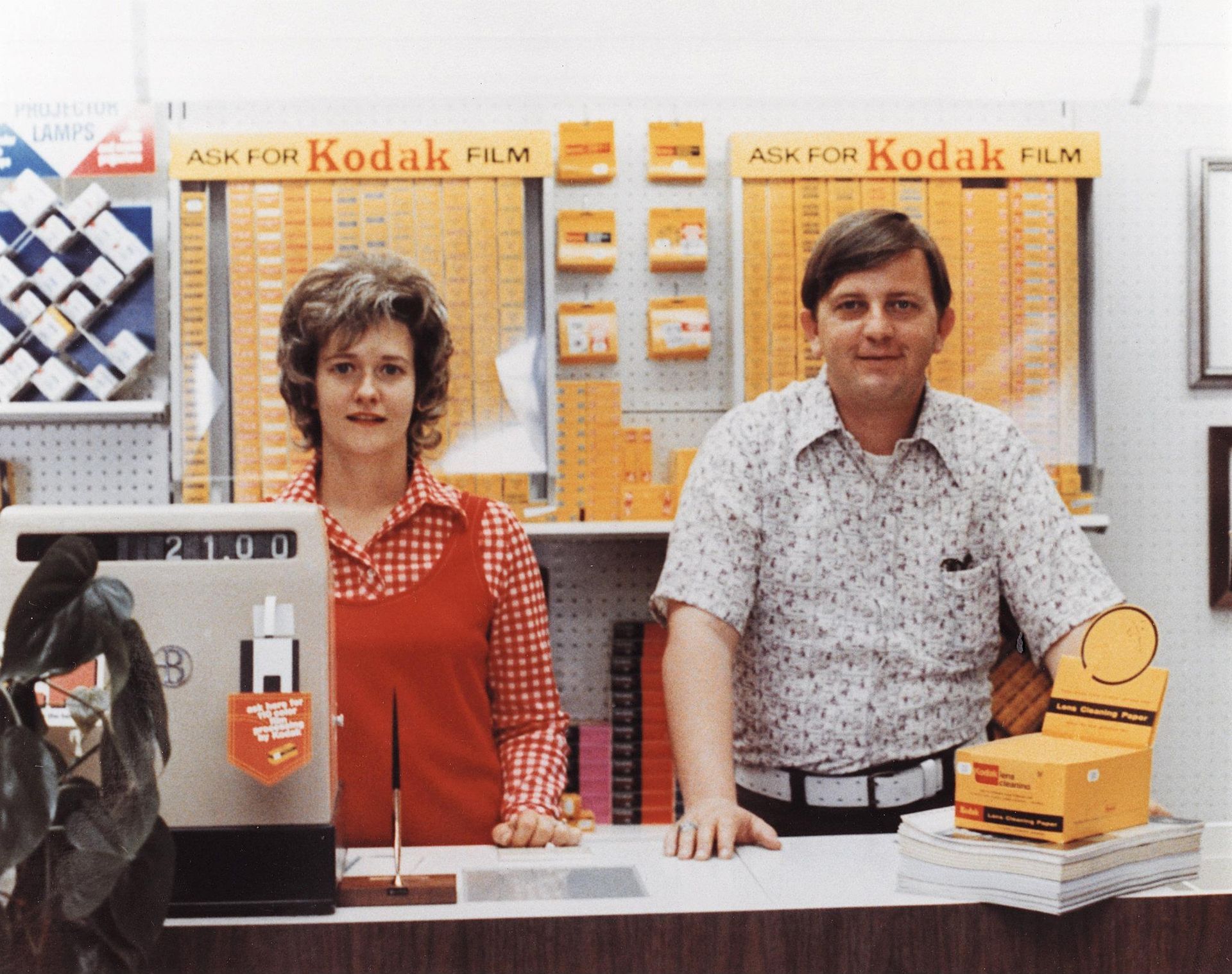 Two employees behind a Kodak film counter with product displays and a cash register