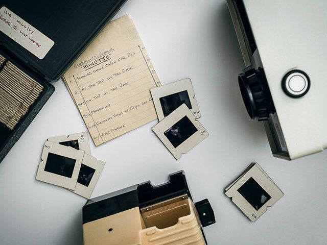 Scattered vintage slide frames and papers on a desk beside a projector