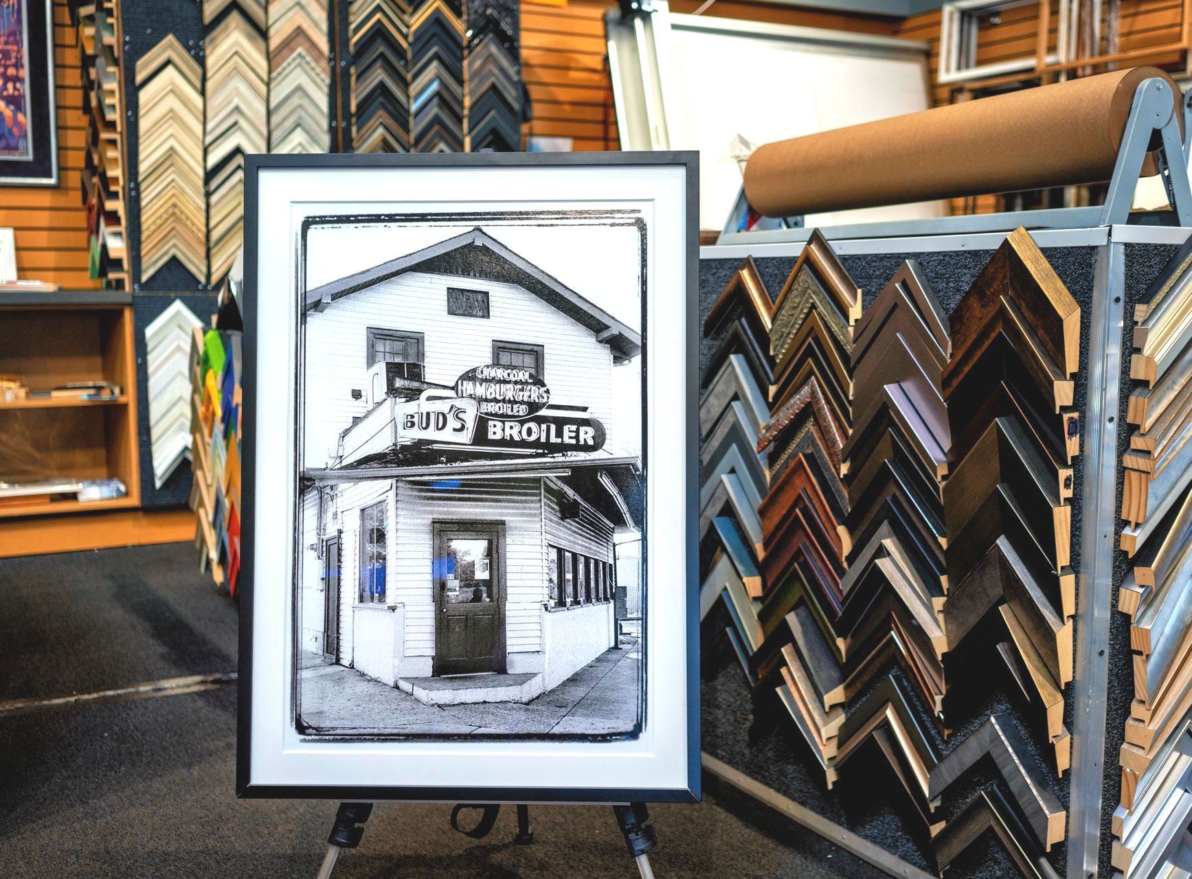 Framed black-and-white storefront sketch displayed in a picture framing shop with sample frames behind it